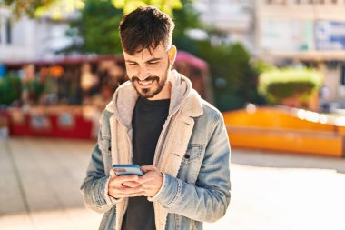 Parkta akıllı telefon kullanarak gülümseyen İspanyol genç adam.