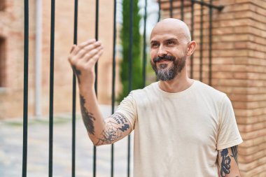 Young bald man smiling confident doing coming gesture with hand at street