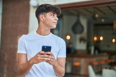 Young hispanic teenager smiling confident using smartphone at street