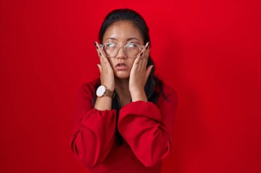 Asian young woman standing over red background tired hands covering face, depression and sadness, upset and irritated for problem 