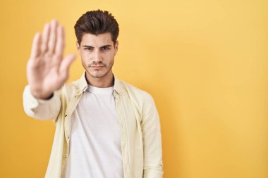 Sarı arka planda duran İspanyol genç adam avucunun içinde şarkı söylemeyi kesiyor. Yüzünde olumsuz ve ciddi bir jest olan uyarı ifadesi. 