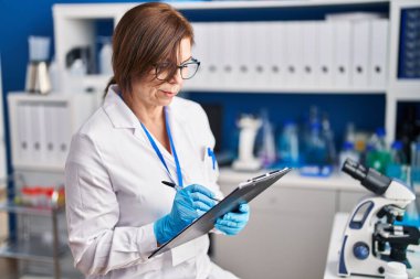 Orta yaşlı kadın bilim adamı, laboratuardaki belgelerde kendinden emin bir şekilde gülümsüyor.