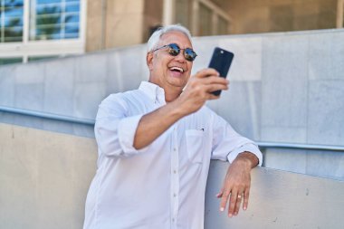 Middle age grey-haired man smiling confident having video call at street