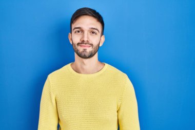 Mavi arka planda duran İspanyol adam yüzünde ciddi bir ifadeyle rahatlamış. Basit ve doğal bir şekilde kameraya bakıyorsun.. 