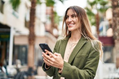 Sokakta akıllı telefon kullanan kendine güvenen genç bir kadın.