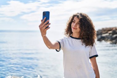 Young hispanic woman smiling confident make selfie by smartphone at seaside