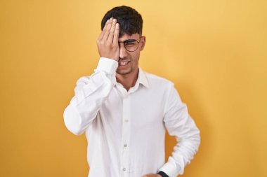 Sarı arka planda dikilen İspanyol genç adam yarı yüzünü, göz ve ağzını eliyle kapatmaktan yoruldu. Yüzüm acıyor.. 