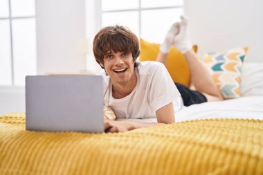 Yatak odasında dizüstü bilgisayar kullanan genç sarışın adam.