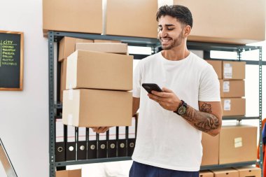 E-ticaret mağazasında akıllı telefon kullanarak karton kutular tutan yakışıklı bir İspanyol.