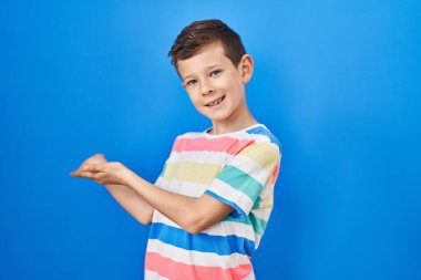 Young caucasian kid standing over blue background inviting to enter smiling natural with open hand 
