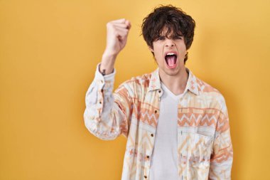 Young man wearing casual summer shirt angry and mad raising fist frustrated and furious while shouting with anger. rage and aggressive concept. 