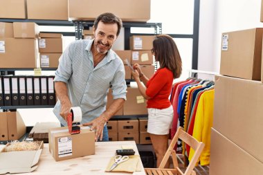 Orta yaşlı erkek ve kadın iş ortakları depoda kendine güvenen paket paketlerine gülümsüyor.