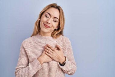 Mavi arka planda duran İspanyol kadın elleri göğsünde, gözleri kapalı ve yüzünde minnet dolu bir jest ile gülümsüyor. sağlık kavramı. 