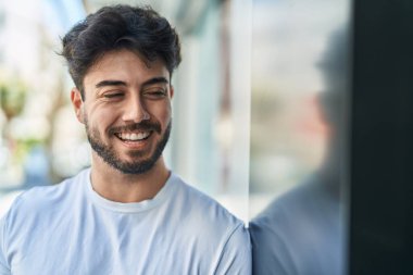 Young hispanic man smiling confident looking to the side at street