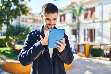Young hispanic man smiling confident using touchpad at park