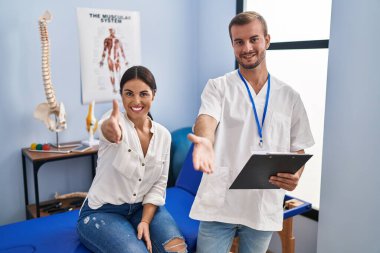 Young hispanic woman at physiotherapist appointment smiling friendly offering handshake as greeting and welcoming. successful business. 