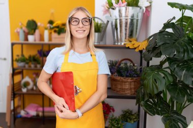 Young blonde woman florist smiling confident holding clipboard at flower shop