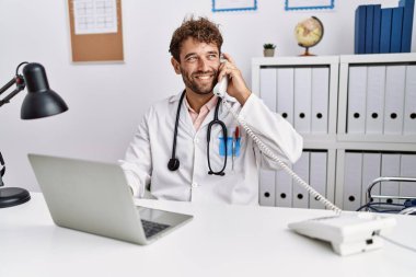 Doktor üniforması giyen İspanyol genç adam klinikte telefonla konuşuyor.
