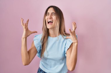 Pembe arka planda duran genç İspanyol kadın kızgın ve deli gibi bağırıyor ve agresif bir ifade ve kollarla bağırıyor. hüsran kavramı. 