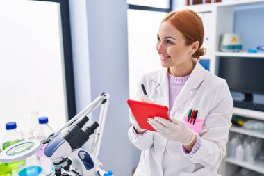 Genç beyaz kadın bilim adamı. Laboratuvarda dokunmatik ped kullanarak gülümsüyor.