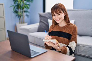 Evde dizüstü bilgisayar kullanan genç bir kadın.