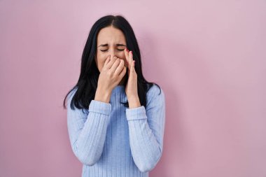 İspanyol kadın pembe arka planda dikiliyor. Pis ve iğrenç bir koku alıyor. Nefesini burnunda tutuyor. Kötü kokuyor. 