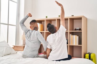 Two men couple waking up stretching arms at bedroom