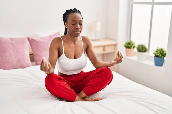 African american woman doing yoga exercise sitting on bed at bedroom