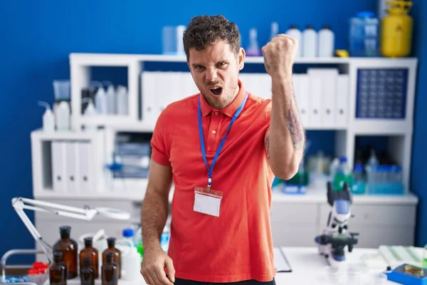 Young Hispanic Man Working Scientist Laboratory Angry Mad Raising Fist — стоковое фото
