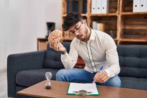 Young Hispanic Man Psychologist Writing Document Holding Brain Psychology Center — Stock Fotó