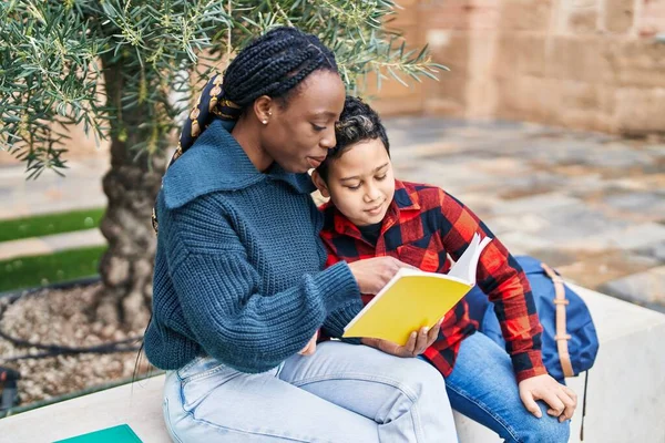 African american mother and son smiling confident reading book at park