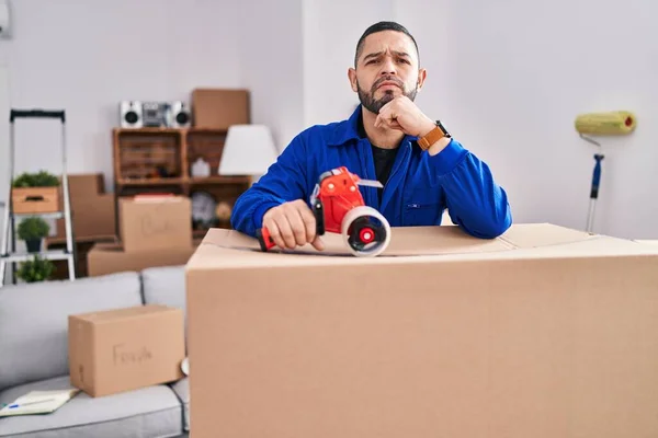 Hispanic Man Working Moving Holding Packing Tape Serious Face Thinking — Foto de Stock