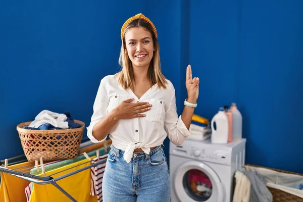 Young Blonde Woman Laundry Room Smiling Swearing Hand Chest Fingers — Stockfoto