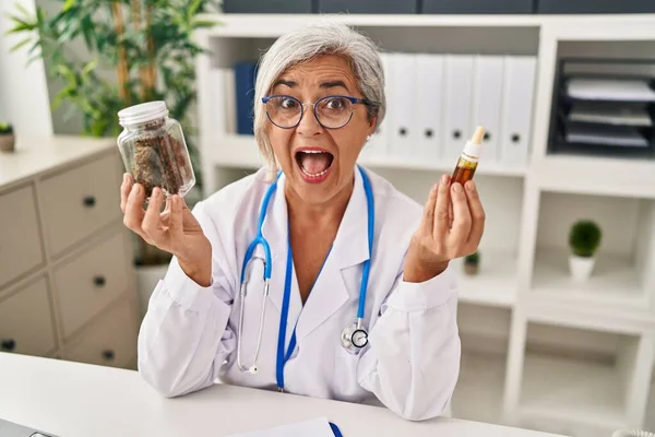 Middle age woman doctor holding cbd oil celebrating crazy and amazed for success with open eyes screaming excited.