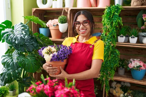 Young arab woman working at florist shop holding plant looking positive and happy standing and smiling with a confident smile showing teeth 