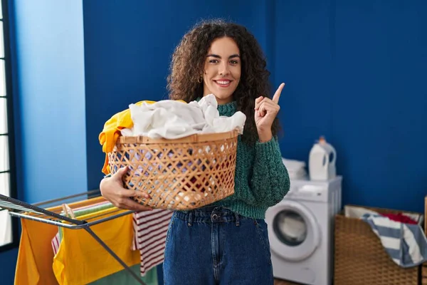 Ung Latinamerikansk Kvinna Håller Tvättkorg Ler Glad Pekar Med Hand — Stockfoto