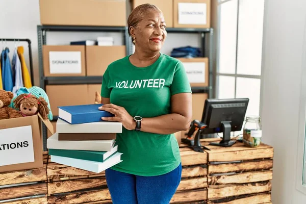 Mujer Afroamericana Mayor Vistiendo Uniforme Voluntario Sosteniendo Libros Centro Caridad — Foto de Stock