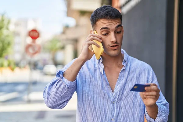 スマートフォンで話してる若いヒスパニック系の男ストリートでクレジットカードを使ってる — ストック写真