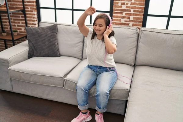 Down syndrome woman listening to music and dancing sitting on sofa at home