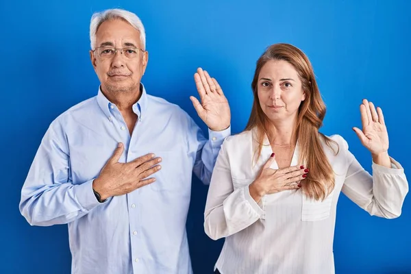 Middle Age Hispanic Couple Standing Blue Background Swearing Hand Chest — Stock Photo, Image
