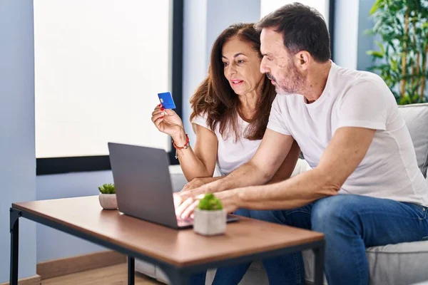 Middle age man and woman couple using laptop and credit card sitting on sofa at home