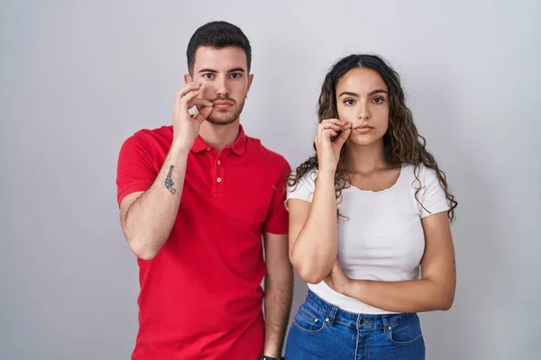 Young Hispanic Couple Standing Isolated Background Mouth Lips Shut Zip — Zdjęcie stockowe