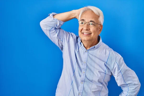Hispanic senior man wearing glasses smiling confident touching hair with hand up gesture, posing attractive and fashionable