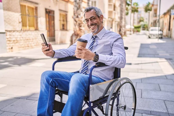 Middle age hispanic man sitting on wheelchair using smartphone at street