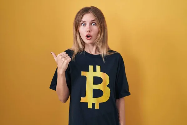 Blonde Caucasian Woman Wearing Bitcoin Shirt Surprised Pointing Hand Finger — Zdjęcie stockowe