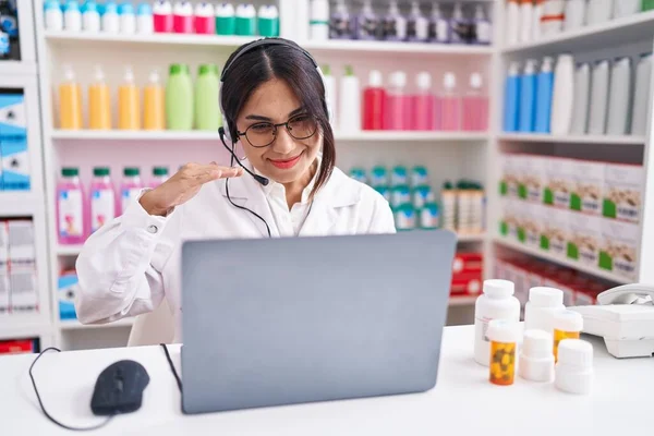 Young arab woman working at pharmacy drugstore using laptop gesturing with hands showing big and large size sign, measure symbol. smiling looking at the camera. measuring concept.