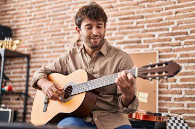 Young man musician smiling confident playing classical guitar at music studio clipart