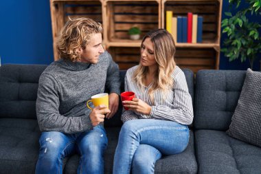 Kadın ve erkek evdeki kanepede oturup kahve içiyorlar.