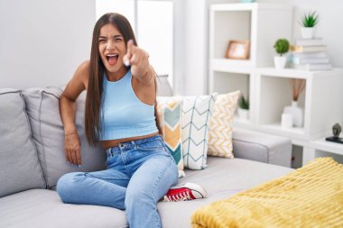 Genç esmer kadın evdeki kanepede oturmuş kameraya kızgın ve sinirli bir şekilde seni işaret ediyor. 