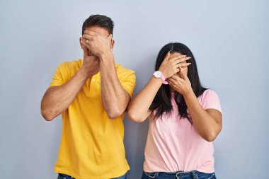 İzole edilmiş arka planda duran genç çift gözlerini ve ağzını elleriyle kapatıyor, şaşırmış ve şok olmuş. duygu gizleme 